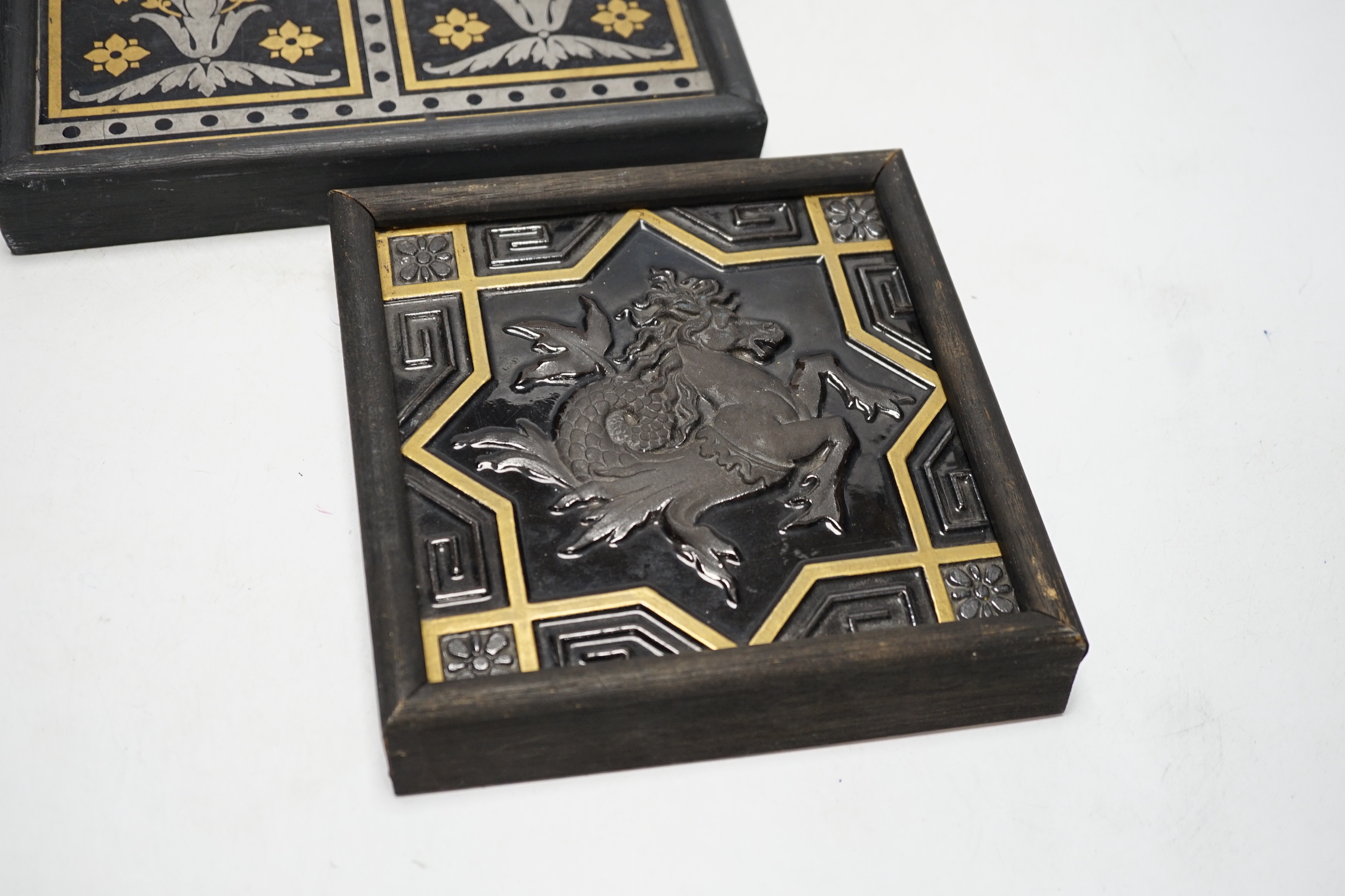 Two Minton tiles comprising one decorated in relief with a Hippocampus and one with geometric floral design, largest overall 22 x 22cm